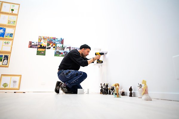 Konstpedagog Peter Anthonsson sätter upp konst på vit vägg.