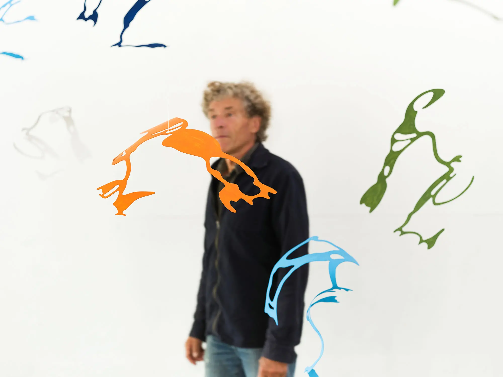 Bengt Håbro bakom sina hängande verk: snirkliga former i orange, blått och grönt