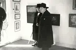 Ett hundra år gammalt foto på två äldre män i långa mörka rockar som står i en konsthall