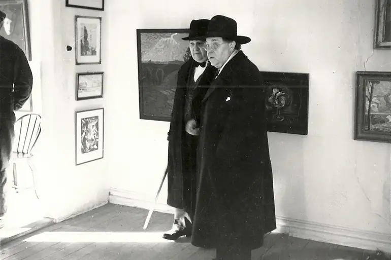 Ett hundra år gammalt foto på två äldre män i långa mörka rockar som står i en konsthall