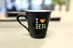Kaffekopp med "I love HR" på skrivbord.